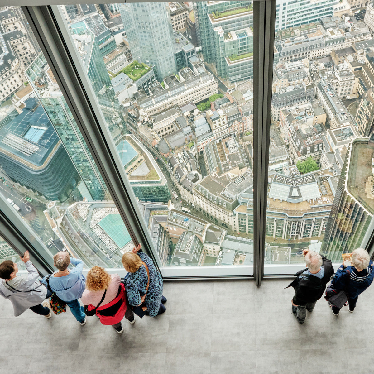 Visitors at a floor-to-ceiling window looking down over London's city rooftops from a skyscraper viewing gallery